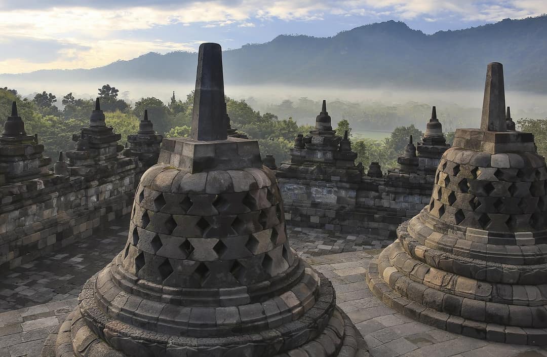 Stupa Candi Borobudur dengan kabut pagi dan pegunungan di belakangnya